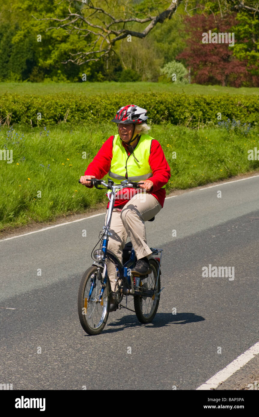 Elderly Woman Female person Lady Cycling Down A Country Lane Road UK Stock Photo