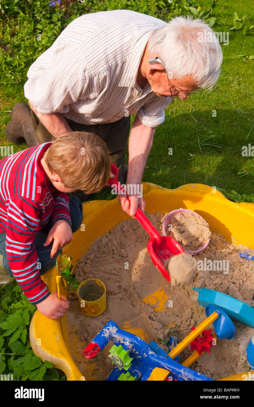 A grandad and his grandson playing in a sandpit in a uk garden Stock Photo