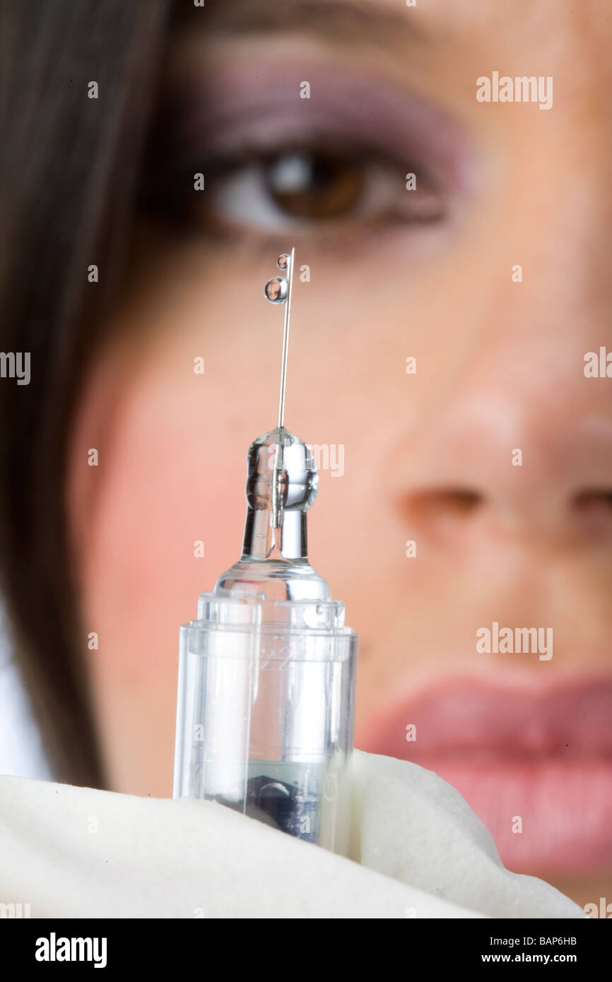 close up shot of syringe with a drop of liquid, nurse with mask in the background Stock Photo