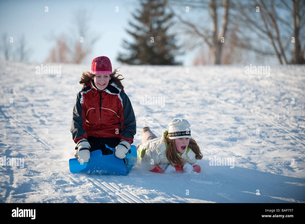 two girls going down tobogganing hill looking scared Stock Photo