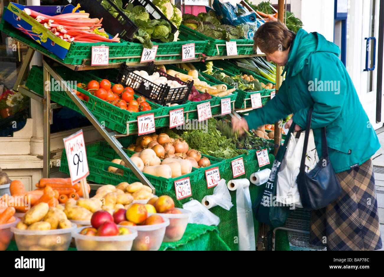 A middle aged woman choosing vegetable produce from the shop front street level display of greengrocer shop or store in England Stock Photo