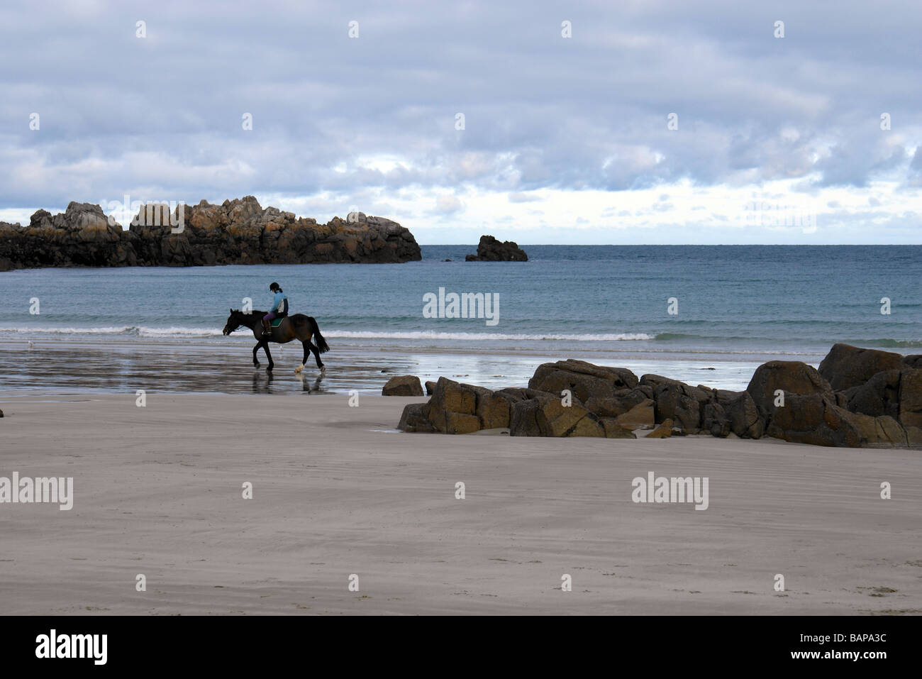 A horse rider trotting along a beach in Guernsey, Channel Islands, UK