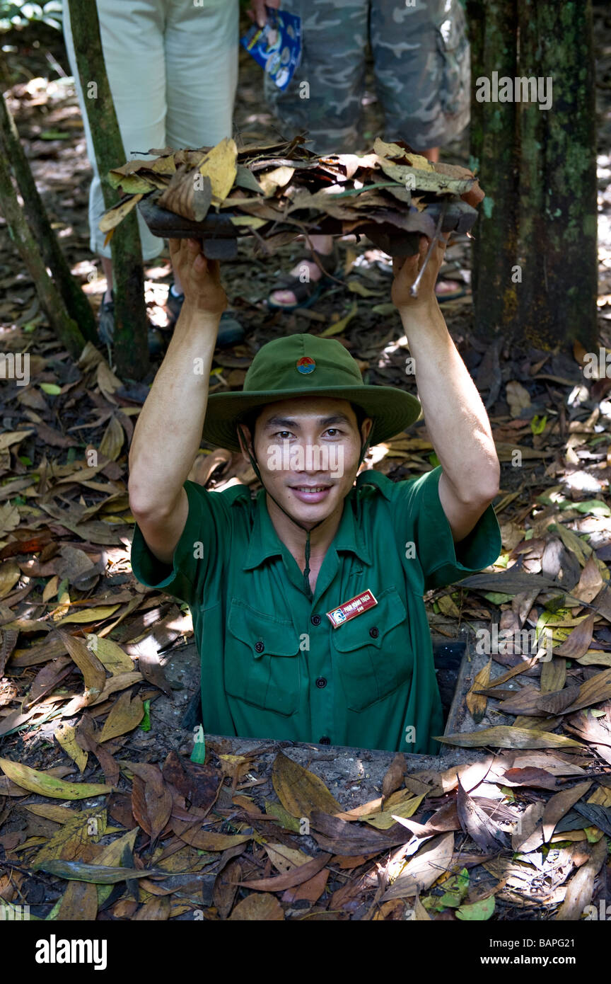 The guide demonstrates tunnel entry and camouflage techniques to tourists. Cu Chi Tunnel Complex, Ho Chi Minh City, Vietnam. Stock Photo