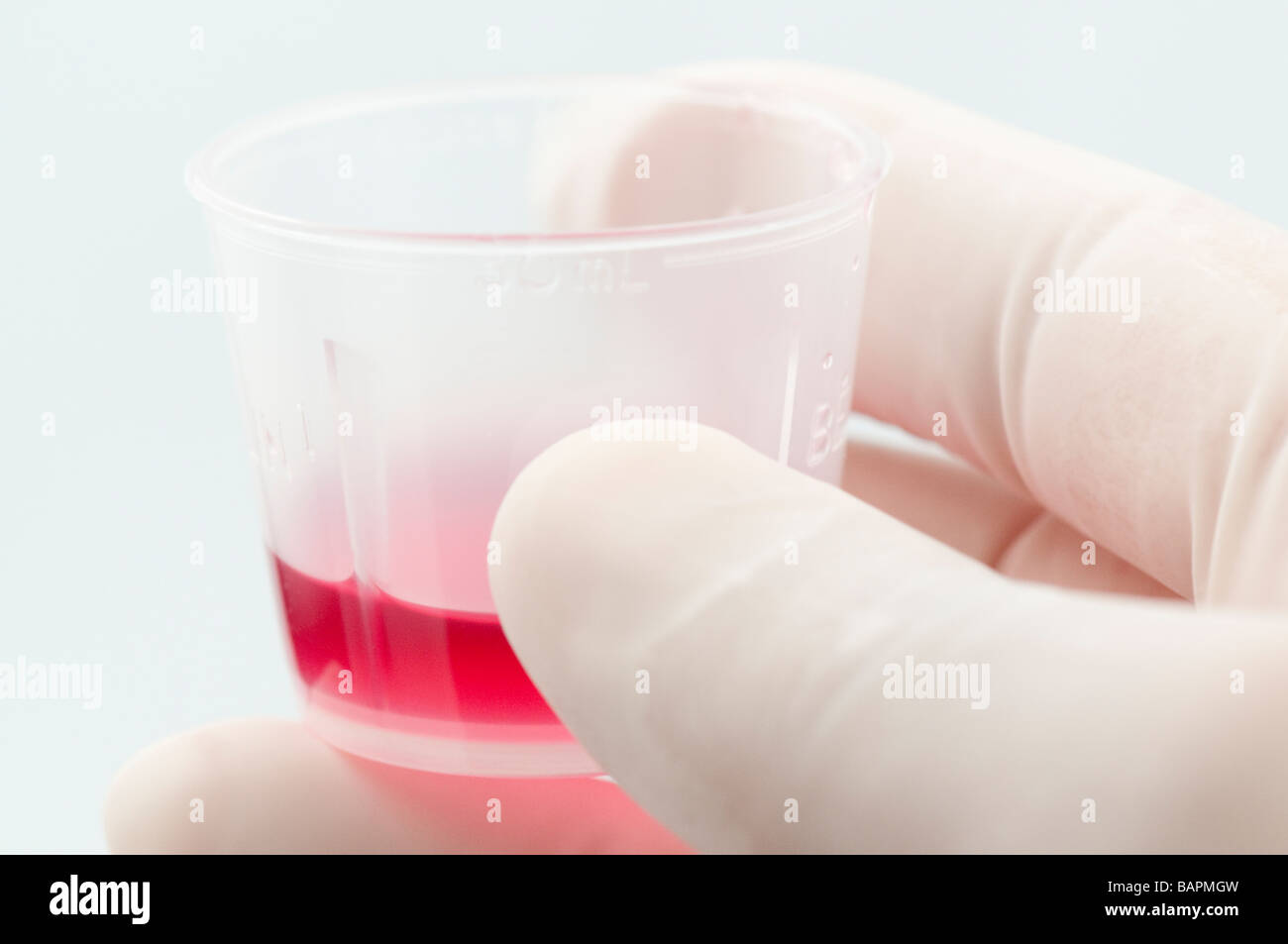 Hand wearing medical latex glove holding cough syrup in measuring cup Stock Photo