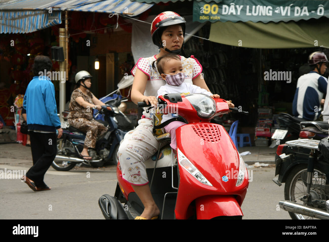 A masked baby on a moped with its mum in Hanoi, Vietnam Stock Photo
