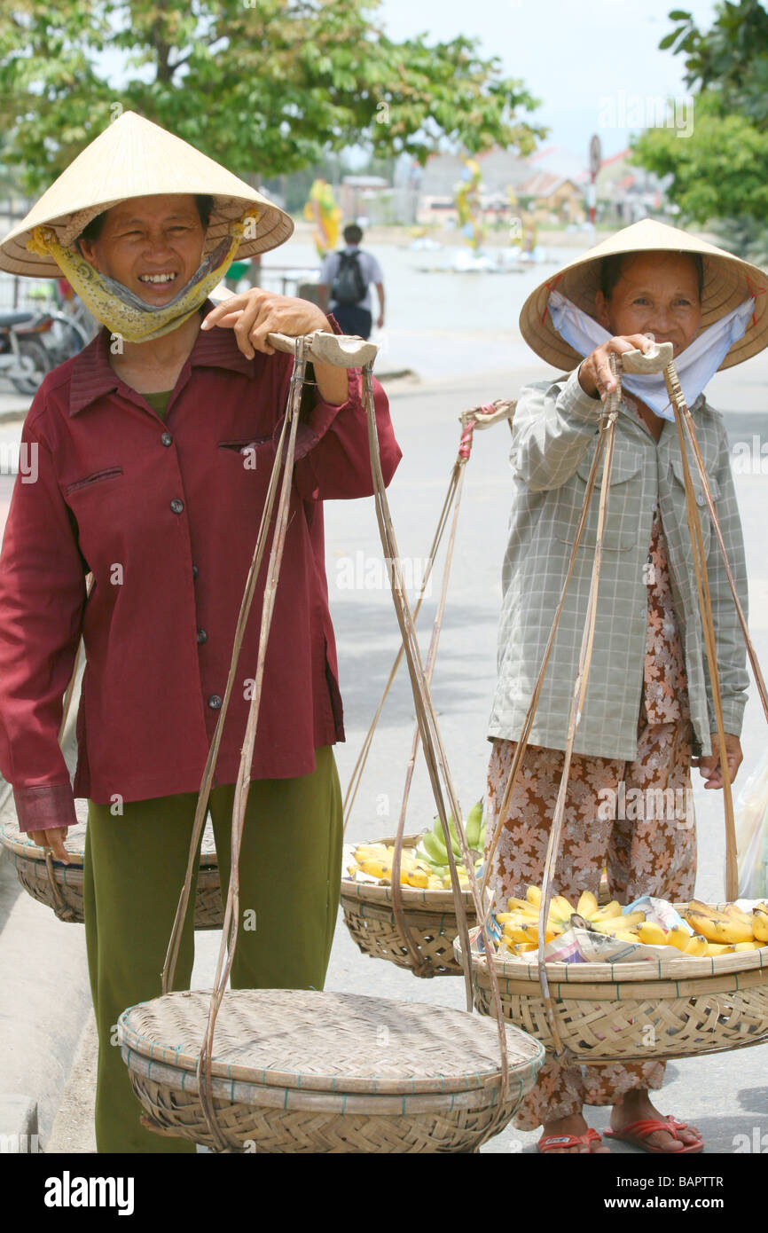 Two female street vendors selling their wares in traditional Vietnamese style in Hoi An, Vietnam Stock Photo