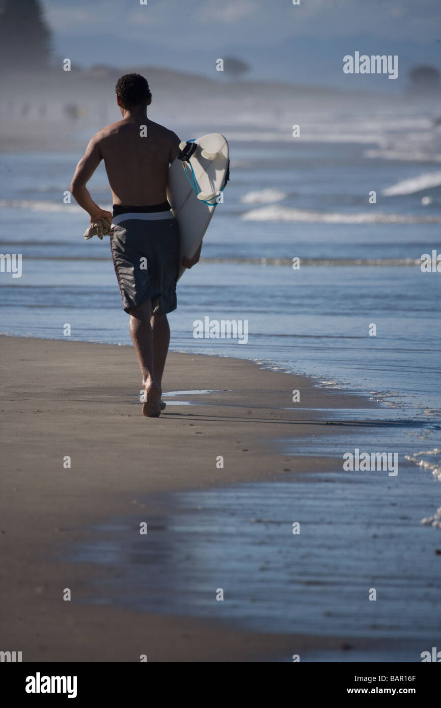Surfer running down Mt Maunganui beach New Zealand Stock Photo