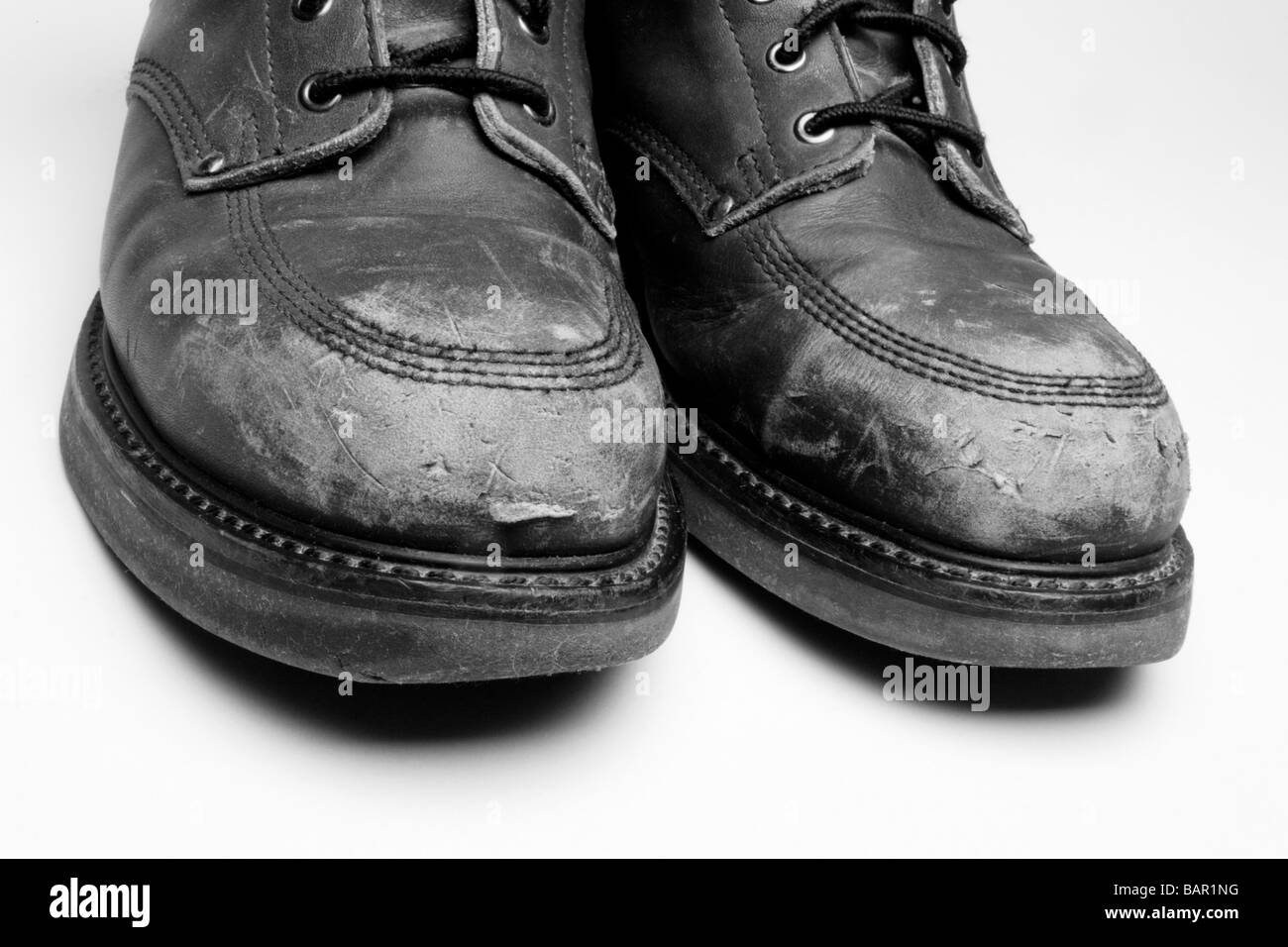 Close-up of scuffed work boots, black and white, isolated on light gray background Stock Photo