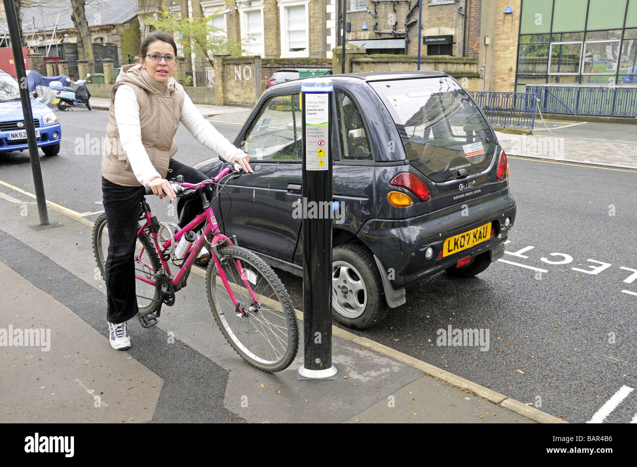 Sustainable transport Women on bike beside electric car which is recharging Highbury Fields Islington London UK Stock Photo
