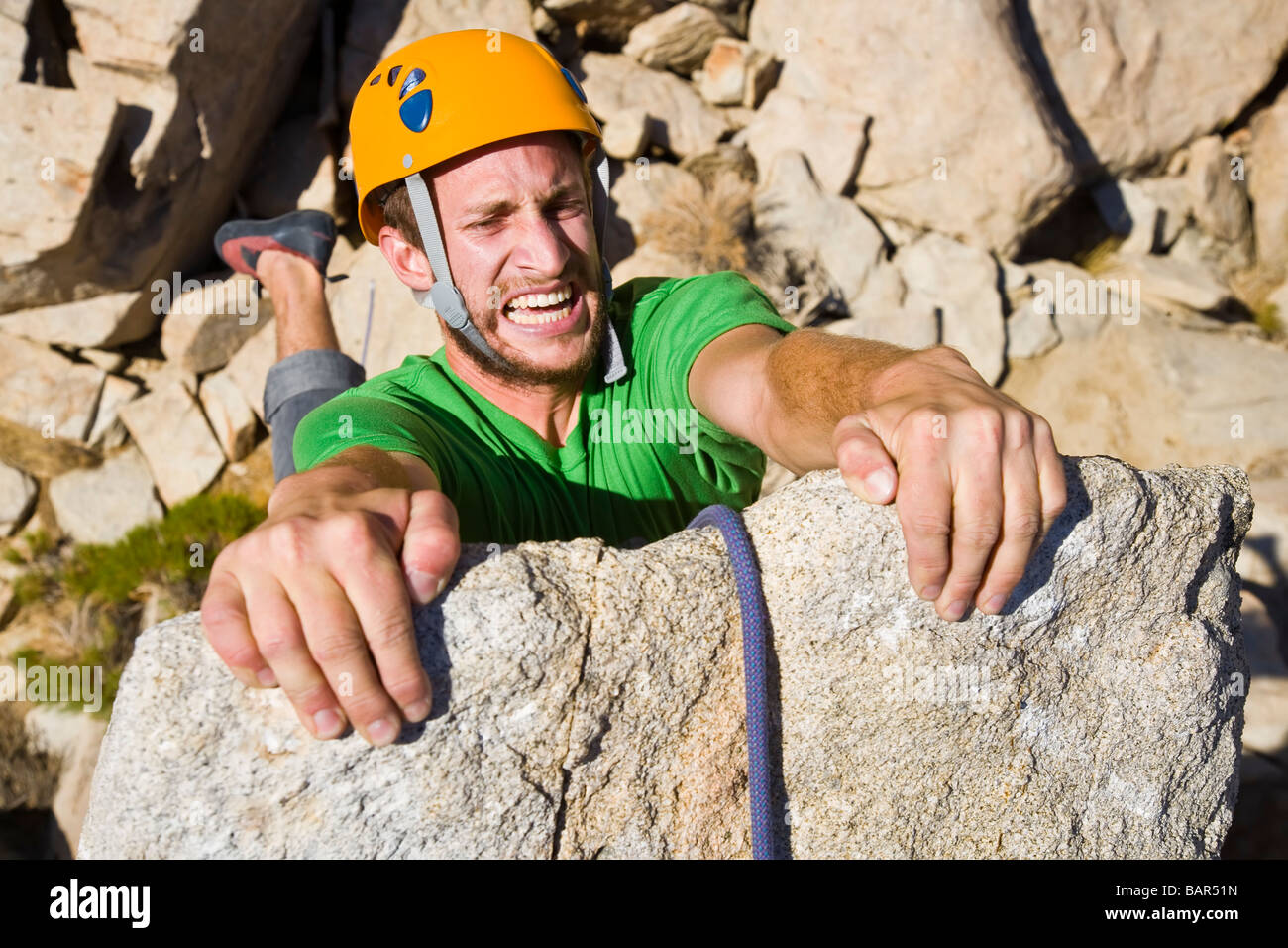 A rock climber desperately clinging to the summit of a rock spire Stock