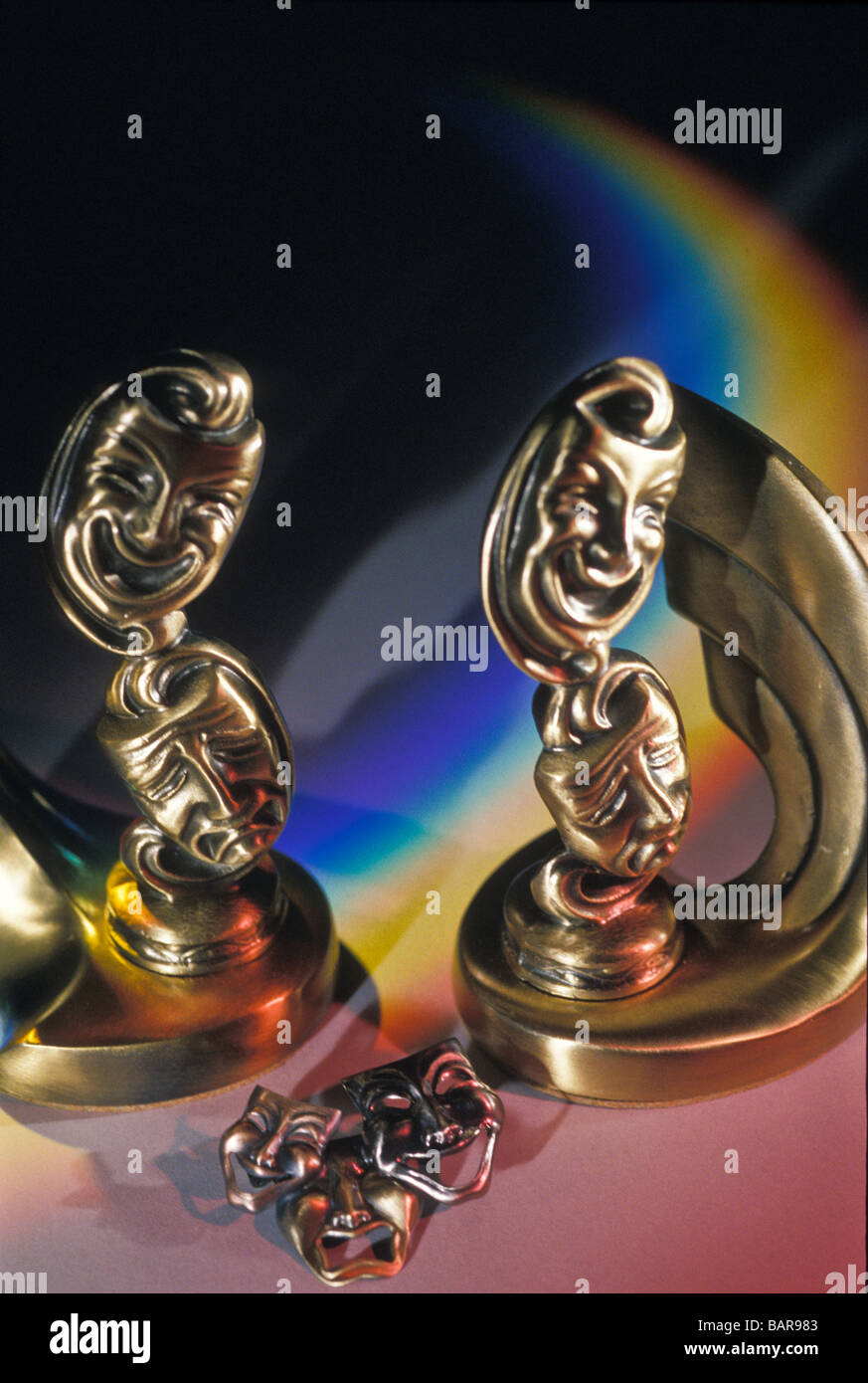 Brass figurines of tragedy and comedy against prjected rainbow of colours background Stock Photo