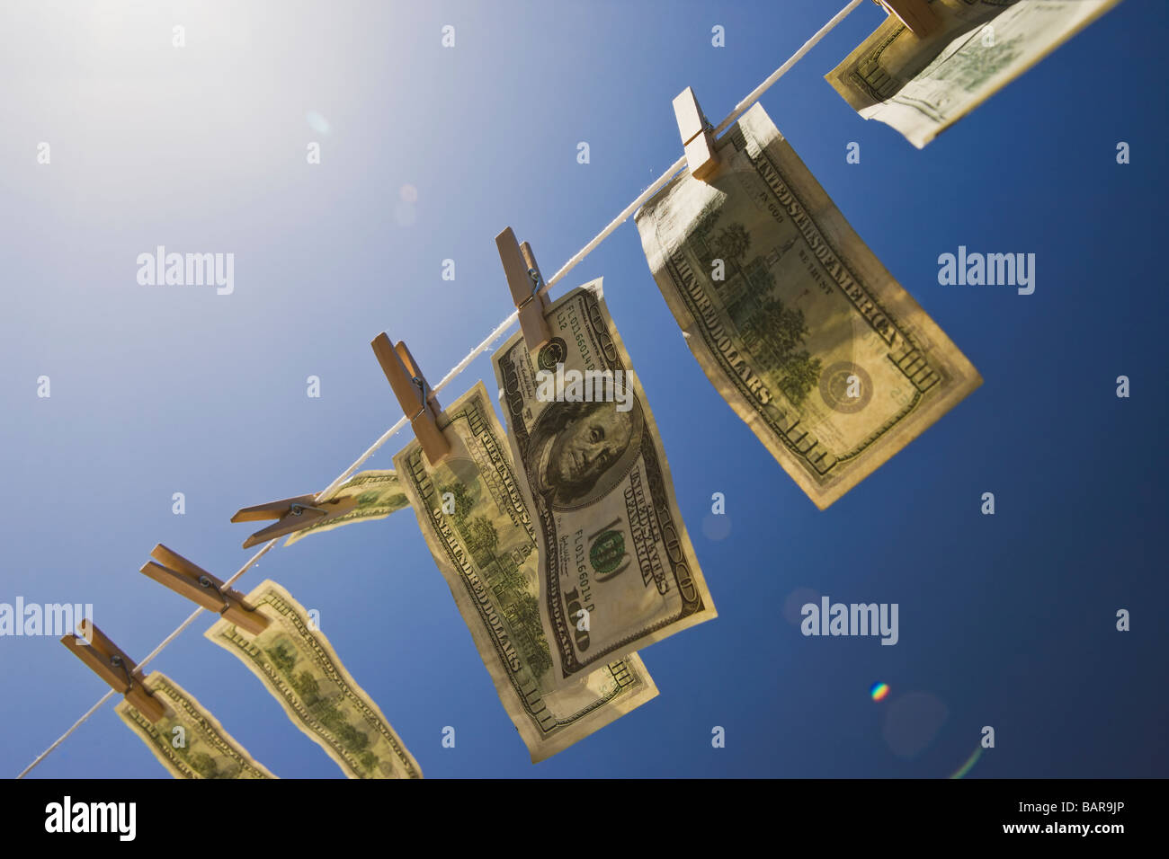 Money Laundering - Dollars: $100 dollar bills drying in the wind under a deep blue sky with intentional lens flare. Stock Photo