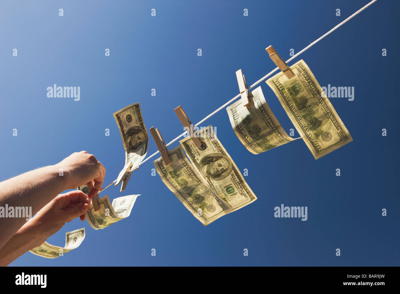 Money Laundering: Hands pinning out $100 dollar bills to dry in the wind under a deep blue sky. Stock Photo
