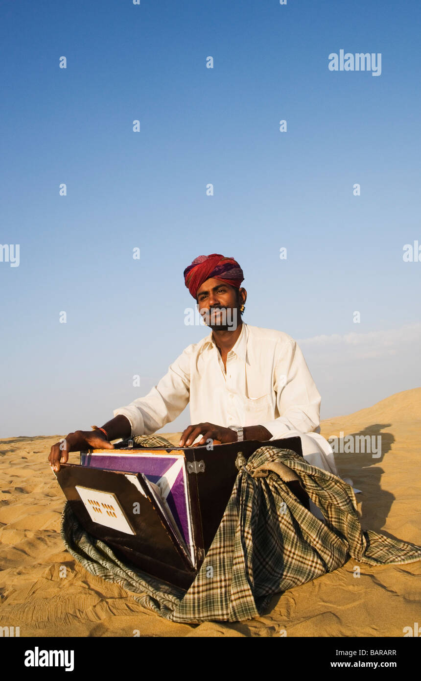 Man playing a harmonium in a desert, Thar Desert, Jaisalmer, Rajasthan, India Stock Photo