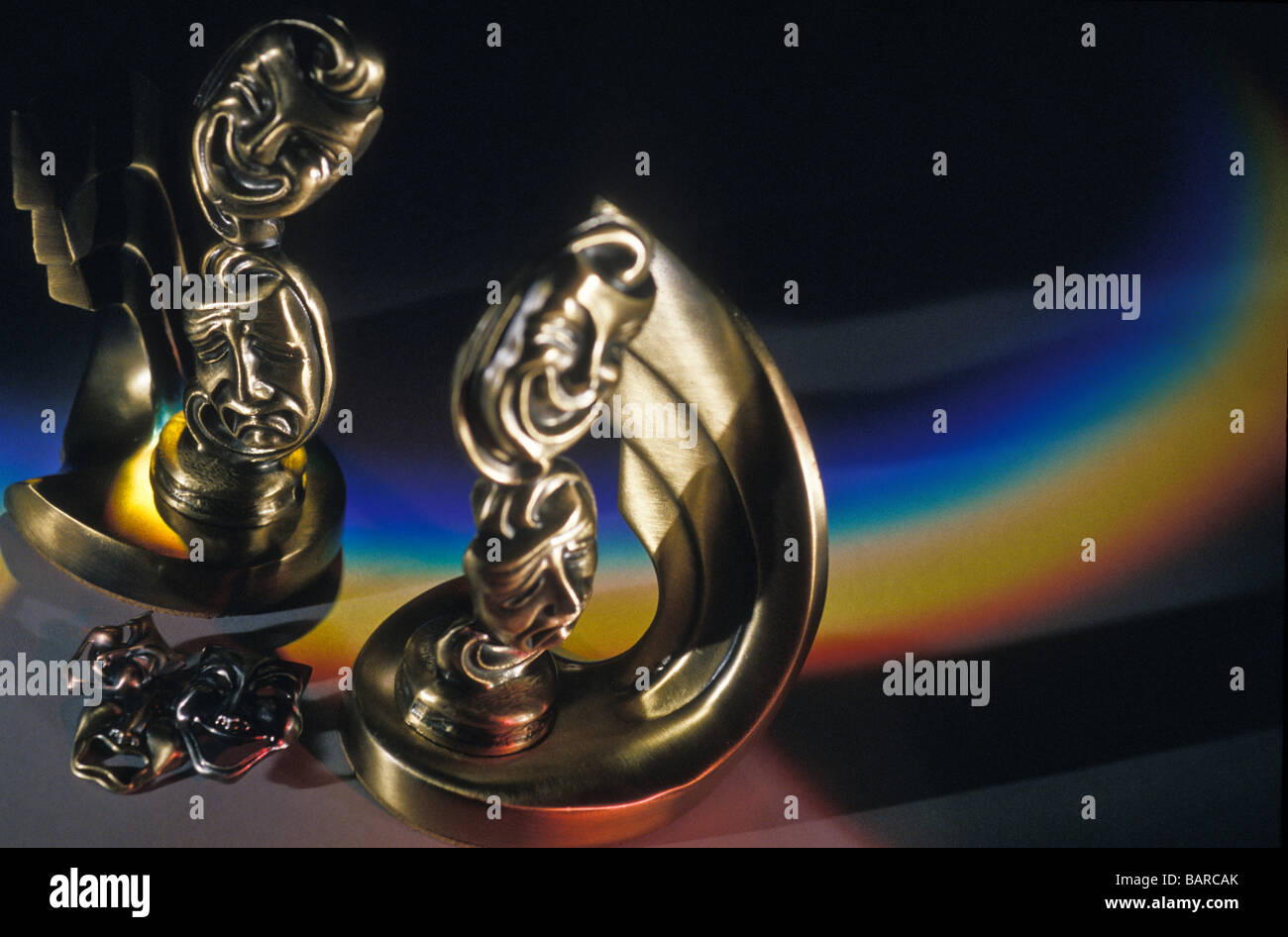Brass figurines of tragedy and comedy against prjected rainbow of colours background Stock Photo