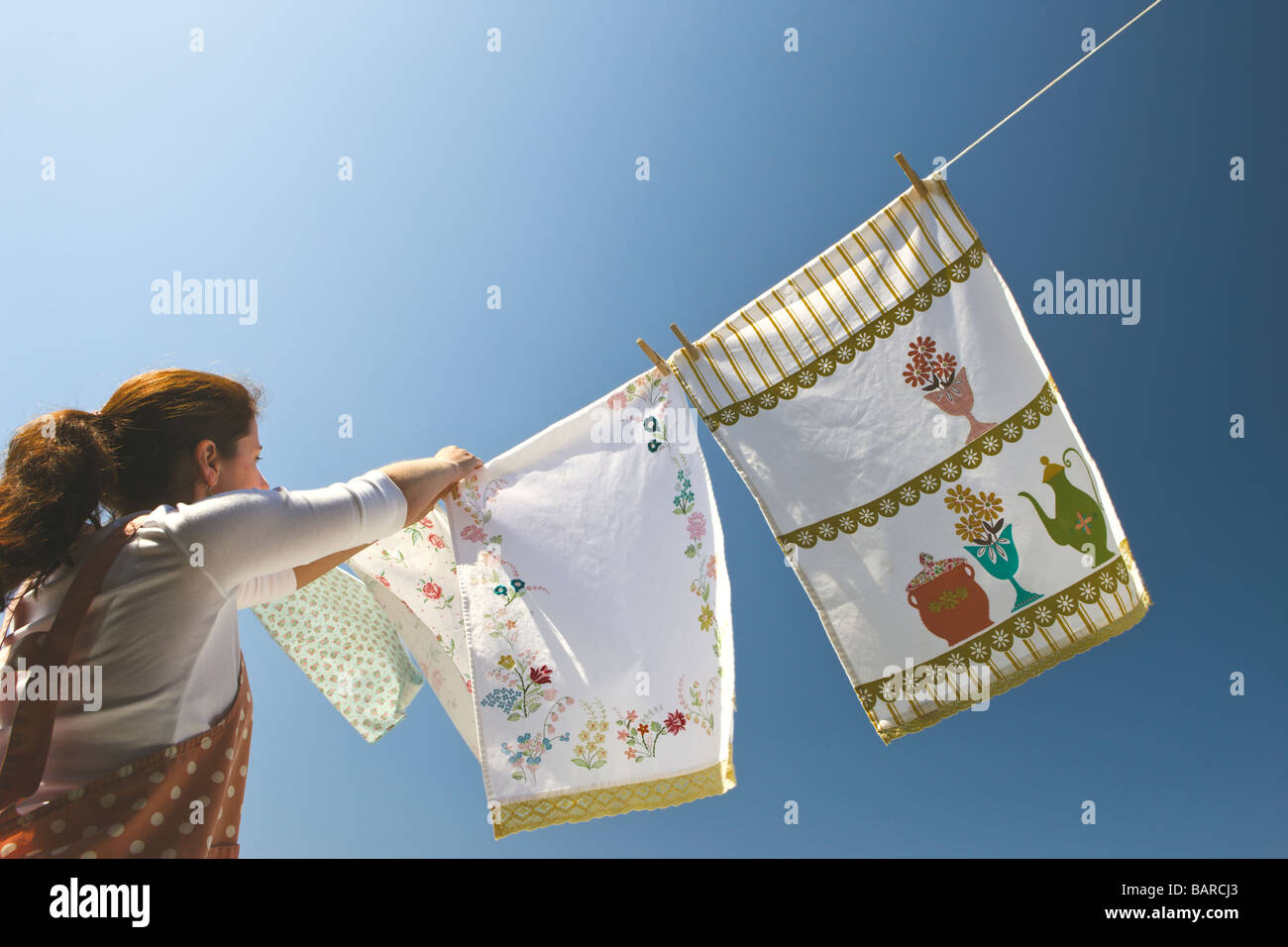 Environmentally friendly: Young woman pinning out colorful washing drying in the wind under a deep blue sky. Stock Photo