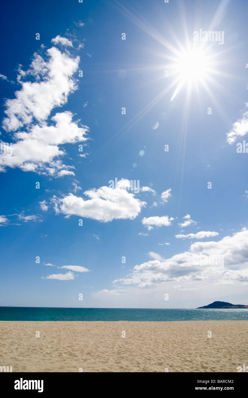 Sun shining on the beach with blue sky and clouds Stock Photo