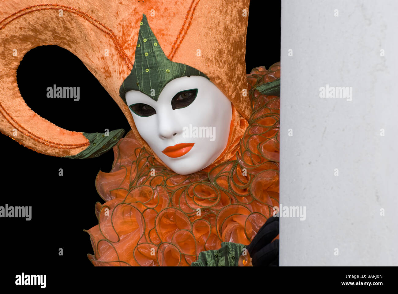 Venice carnival disguise with orange color standing behind a wall Stock Photo