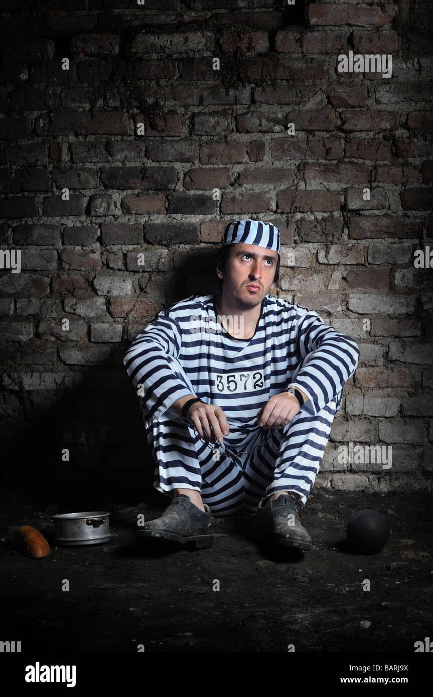 Young prisoner in chains sitting on the floor of a dark prison cell