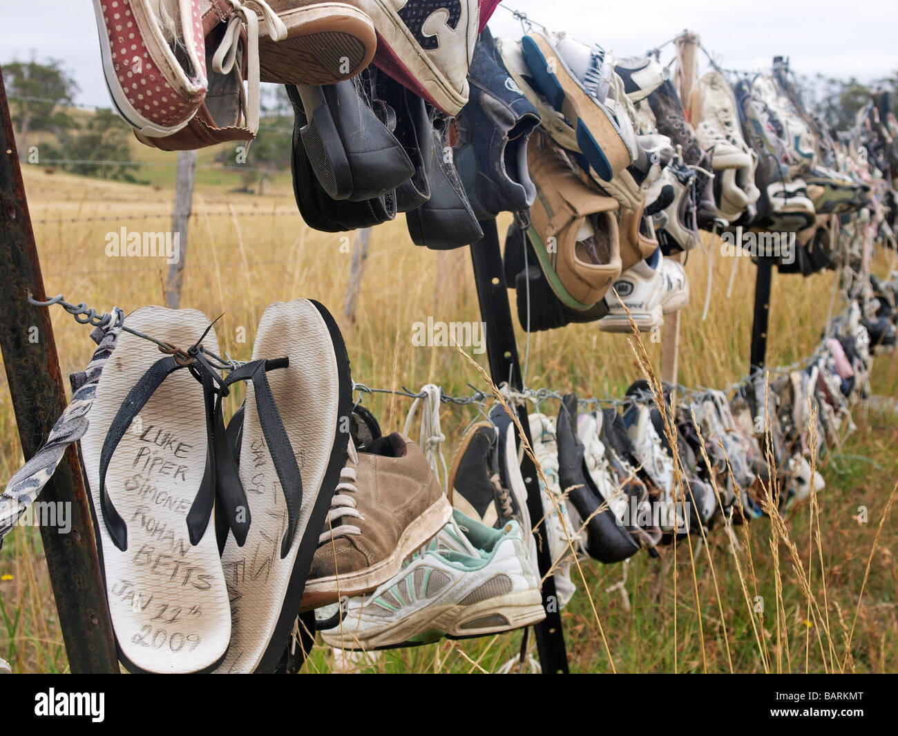 LOST AND ABANDONED TRAINERS, FLIP FLOPS AND SHOES HUNG ON BARBED WIRE FENCE  TASMANIA AUSTRALIA Stock Photo - Alamy