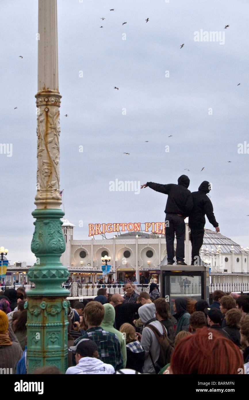 Two people stand on phone box with Palace pier in backgroud during may day protests Brighton, Sussex, UK JPH0201 Stock Photo