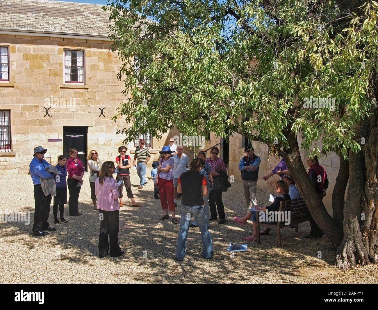 VISITORS LISTEN TO GUIDE WHILST STANDING  IN COURTYARD UNDER SHADE OF TREE OF RICHMOND GAOL TASMANIA AUSTRALIA Stock Photo