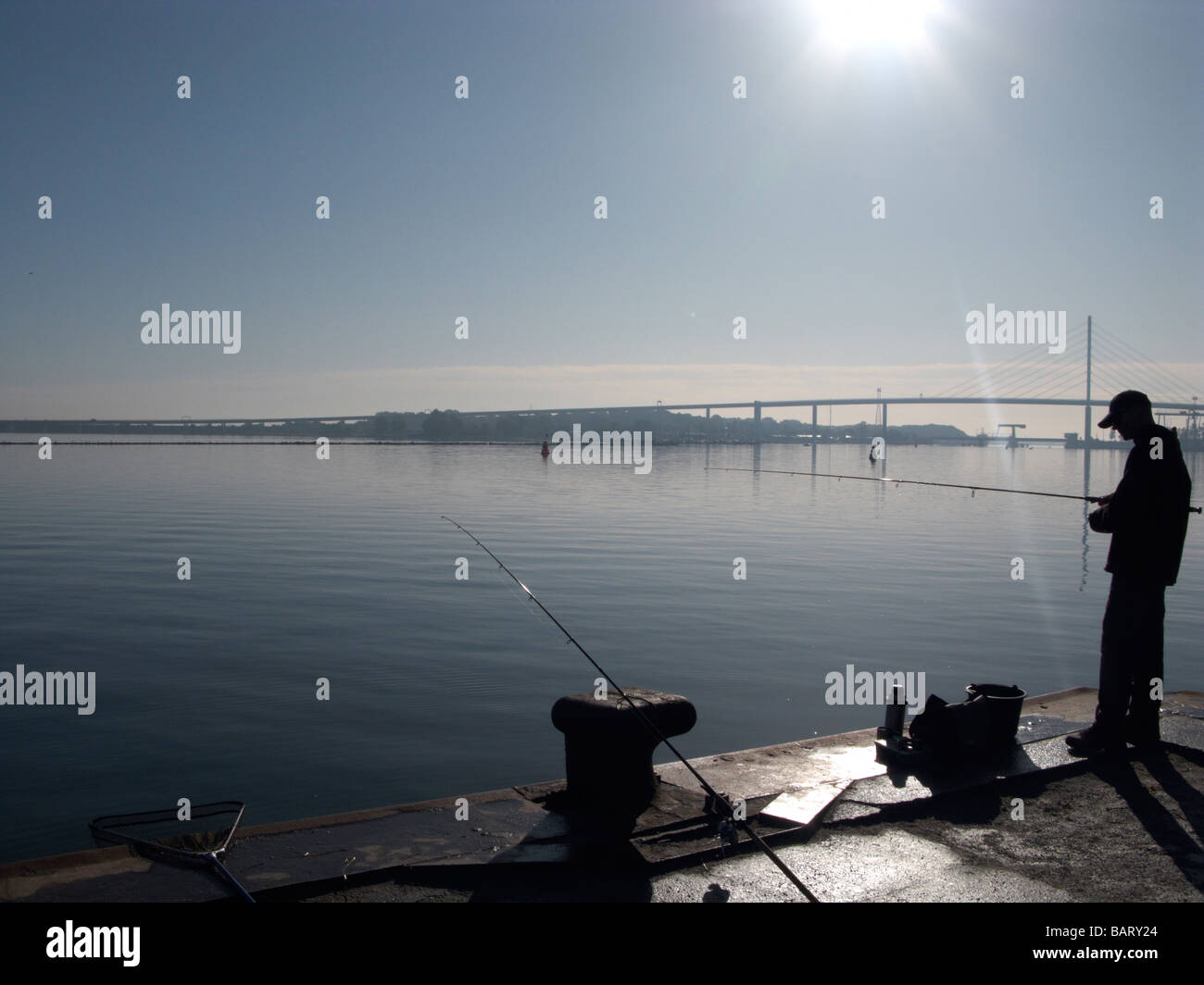 Fisherman silhouette by the sun at the harbour in Stralsund on the Baltic see with Rugen bridge in background Germany Stock Photo