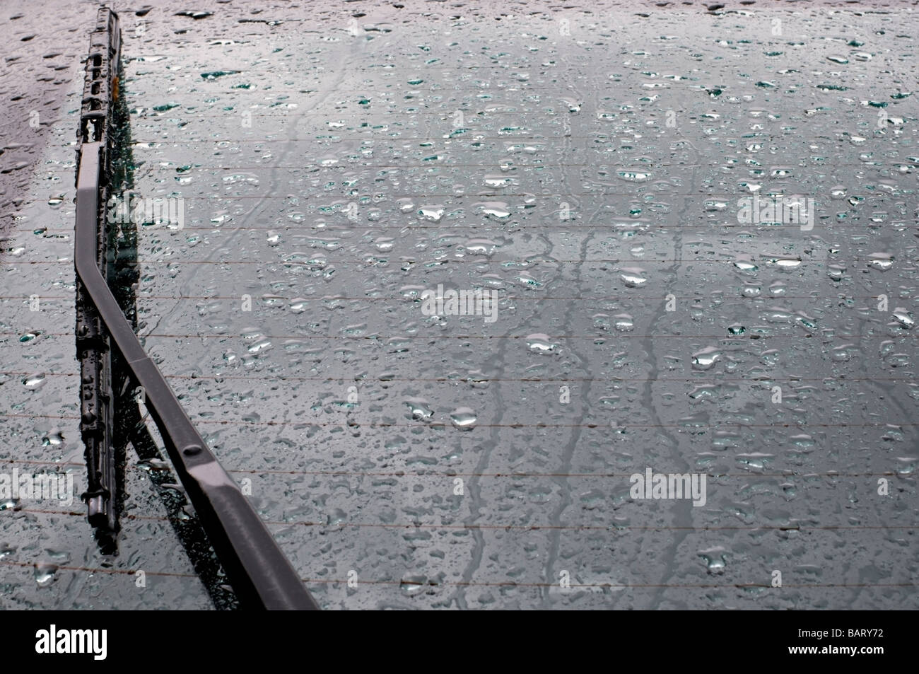 Raindrops and a wiper blade on the back window of a car. Stock Photo