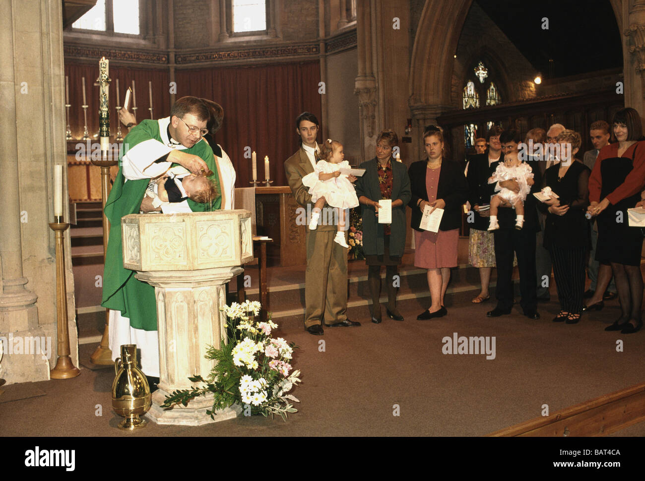 Catholic priest baptising baby at font Stock Photo