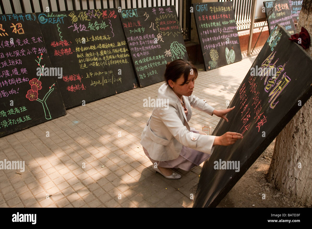 Beijing China A woman writes out the day's menu for her restaurant with coloured chalk on blackboards on the pavement. Stock Photo