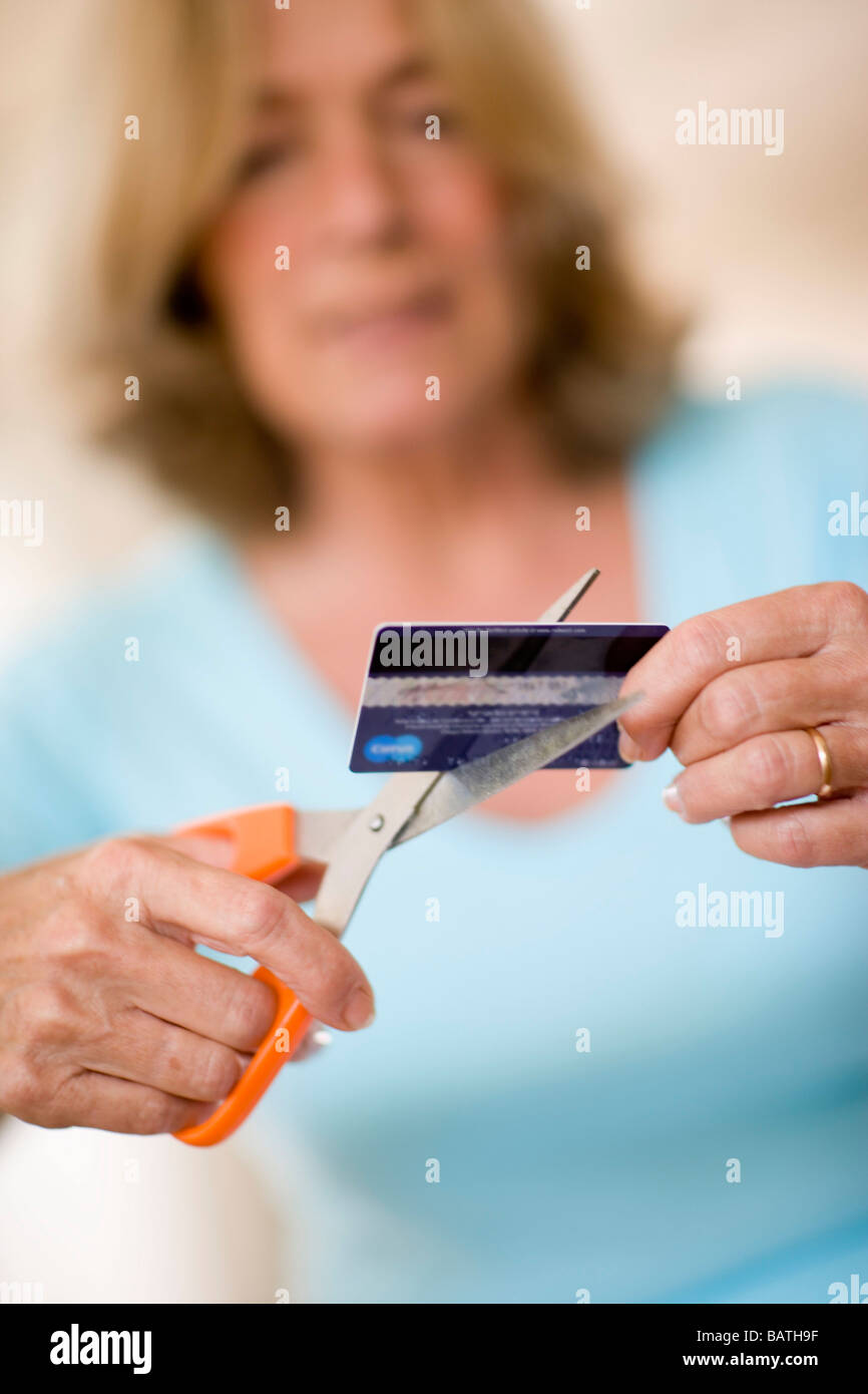 Credit card debt. Woman using a pair of scissors to cut up her credit card. Stock Photo