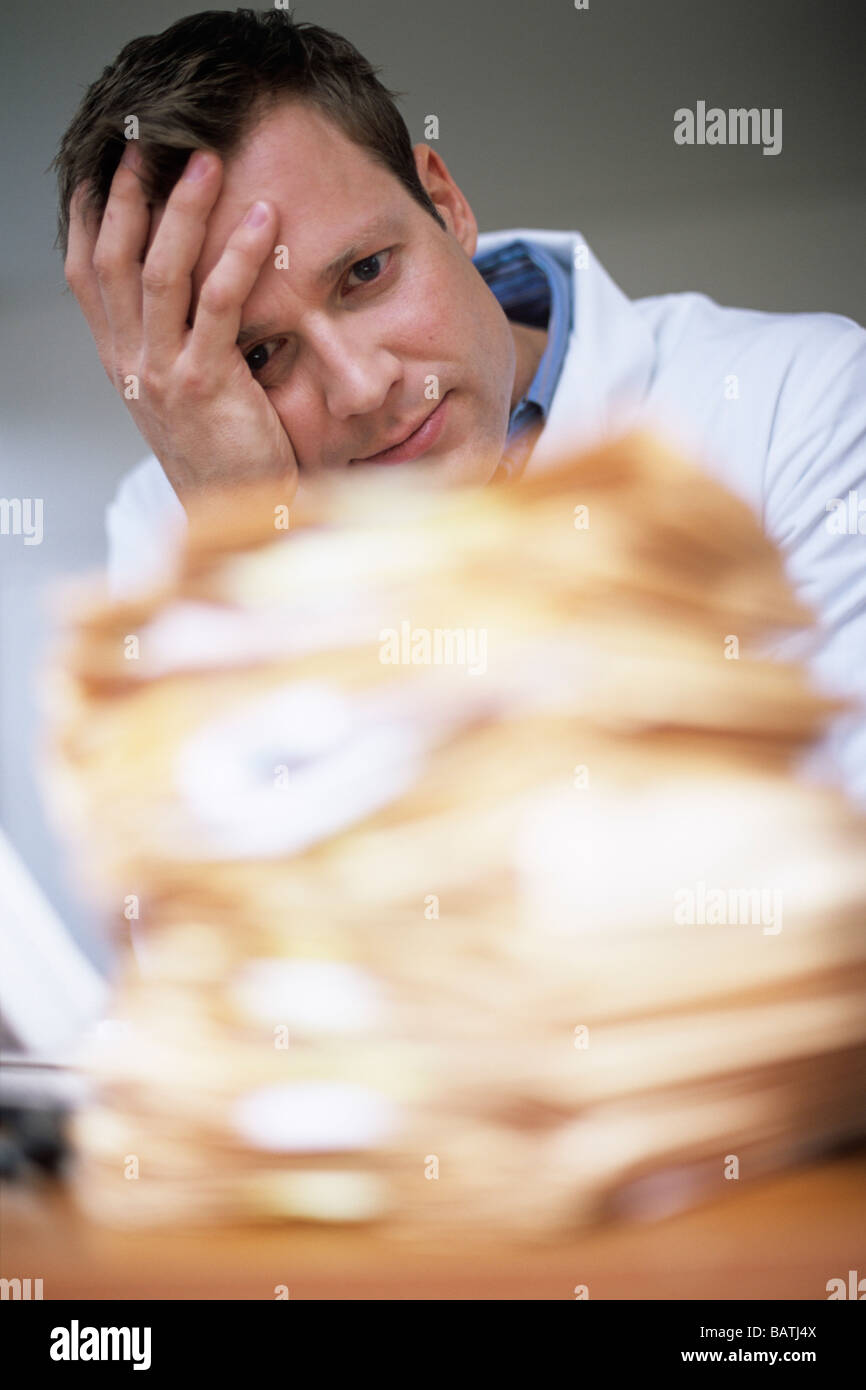 Overworked doctor sitting behind a pile of patient's notes. Stock Photo