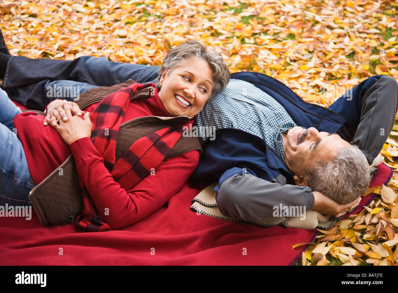 African couple laying on blanket among autumn leaves Stock Photo