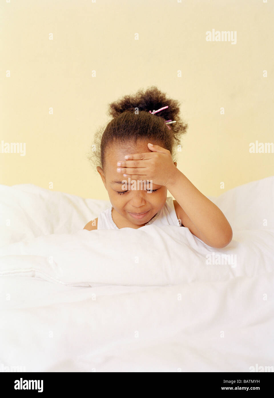 Feverish child. Four-year-oldgirl holding her head. She is in bed with a fever.Fever, known as pyrexia. Stock Photo