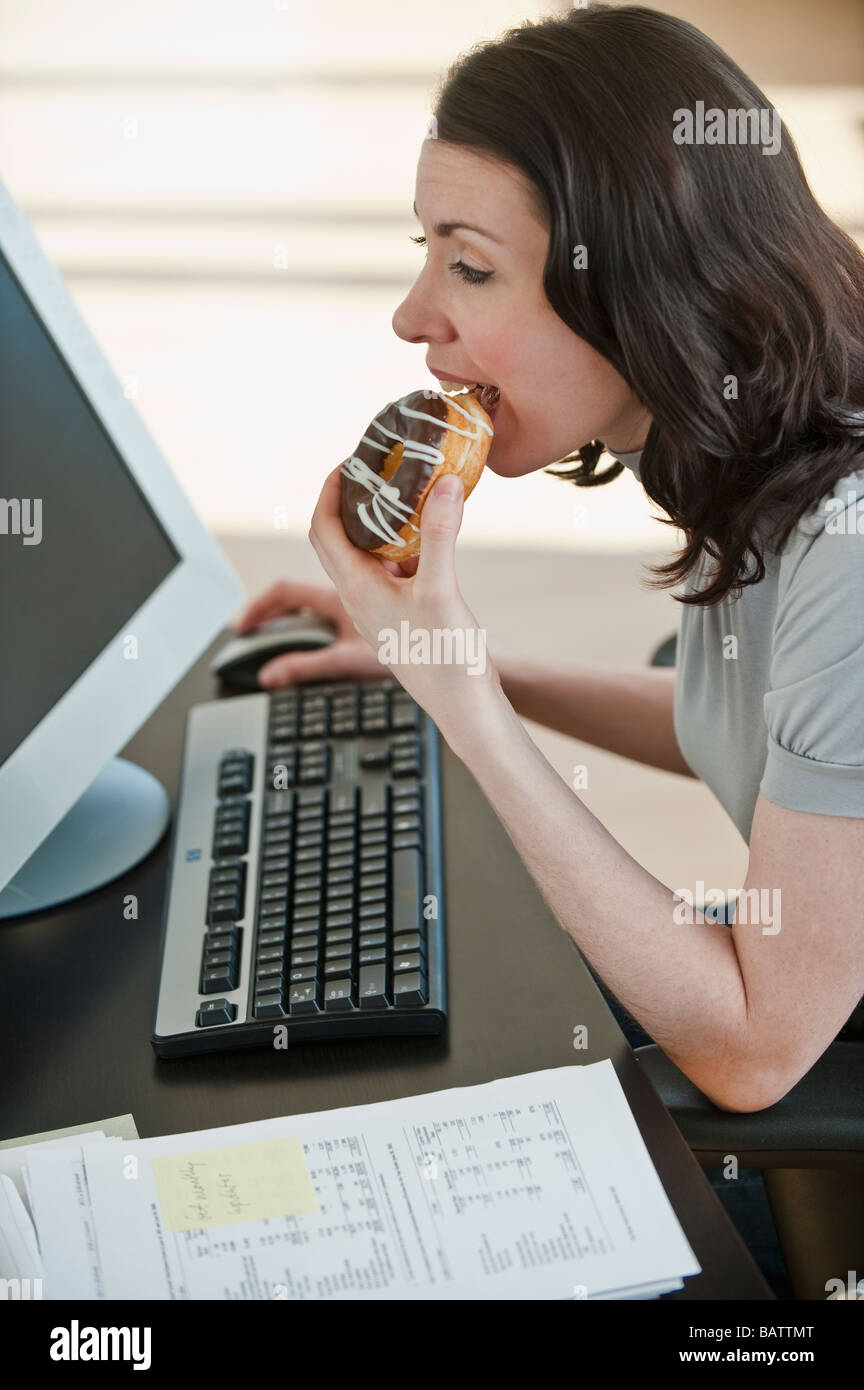Business woman eating donut at desk in office Stock Photo