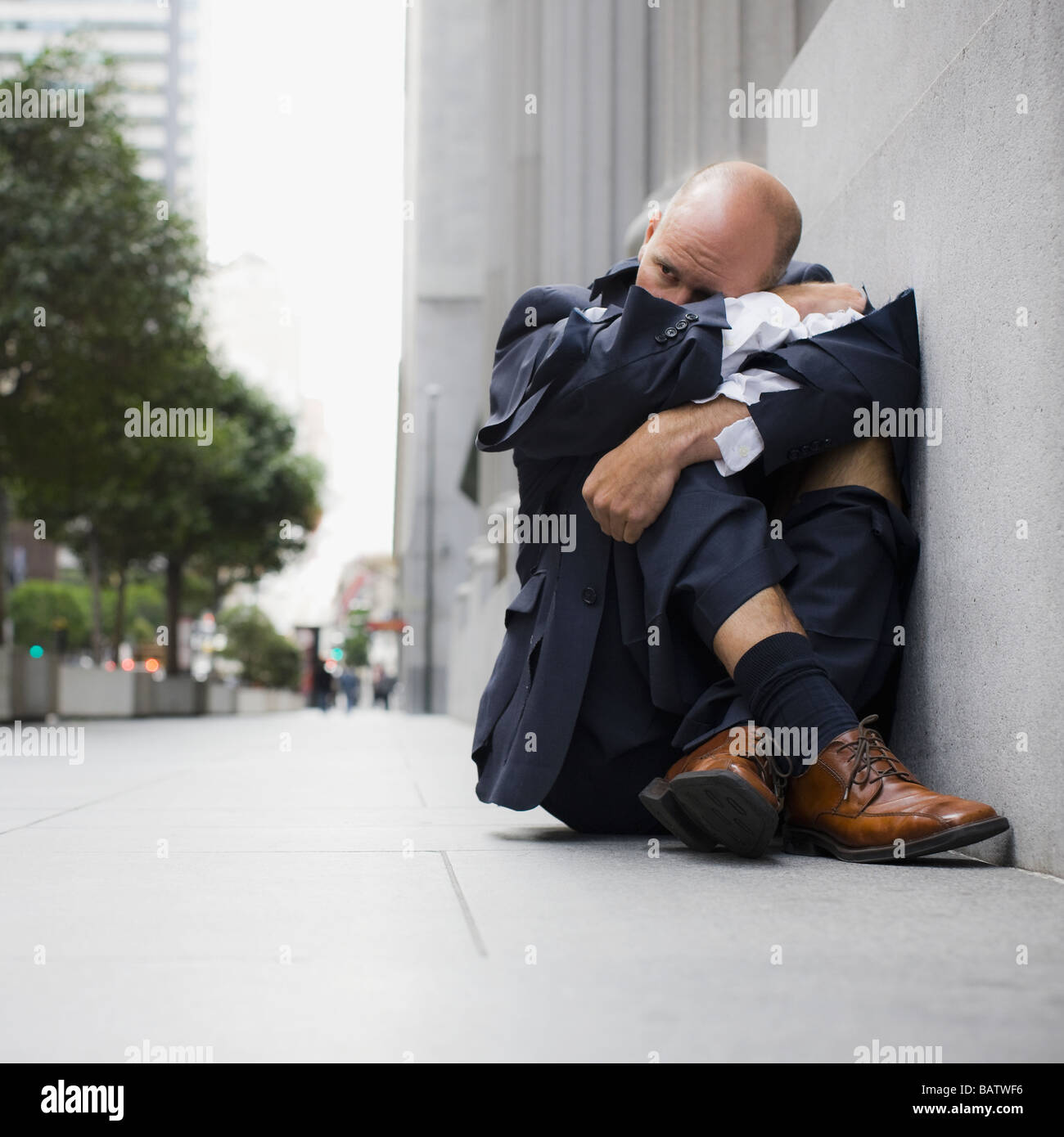 USA, California, San Francisco, Businessman wearing torn clothing, sitting on sidewalk Stock Photo