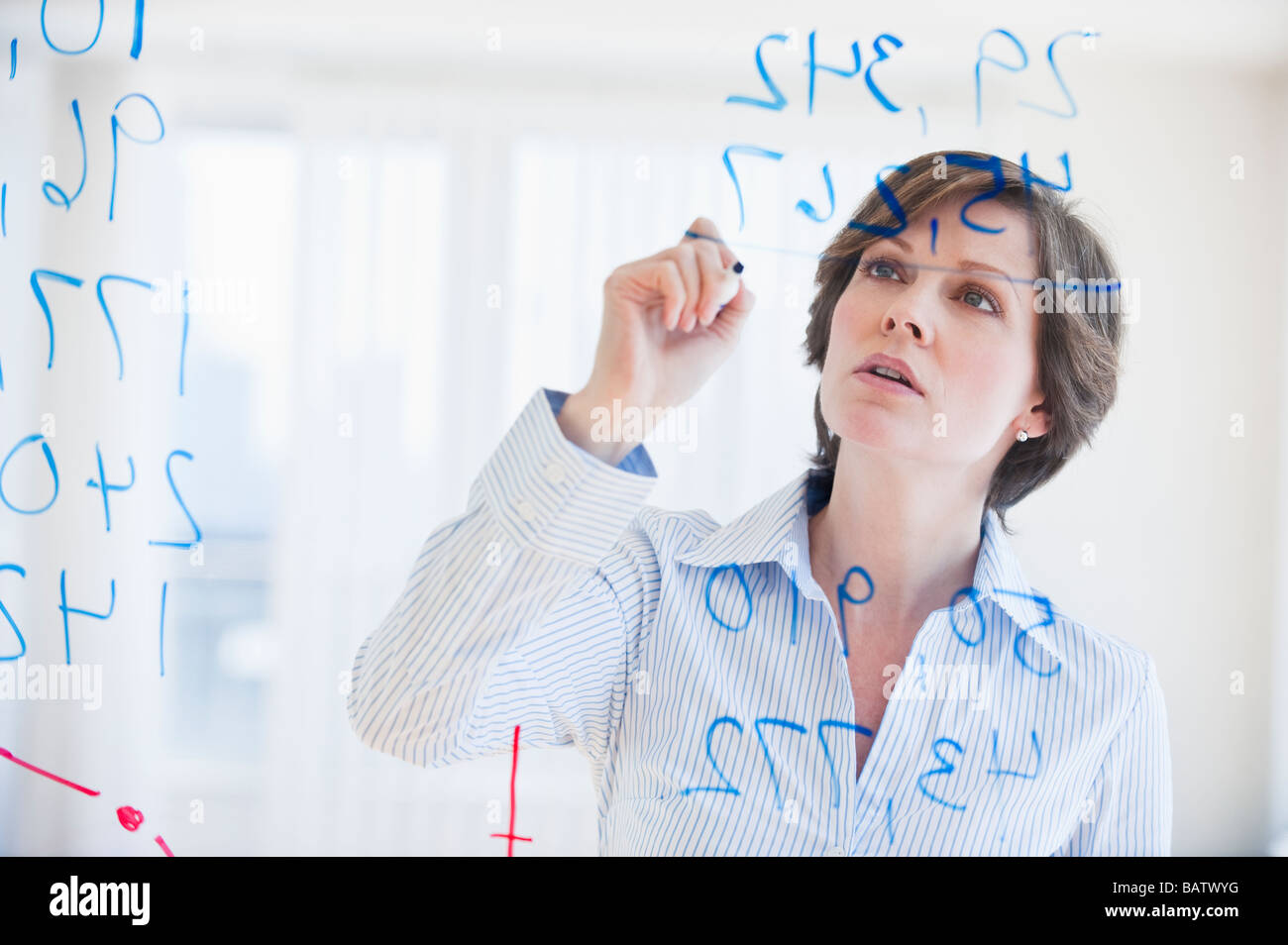 Mature businesswoman writing numbers on transparent glass wall Stock ...