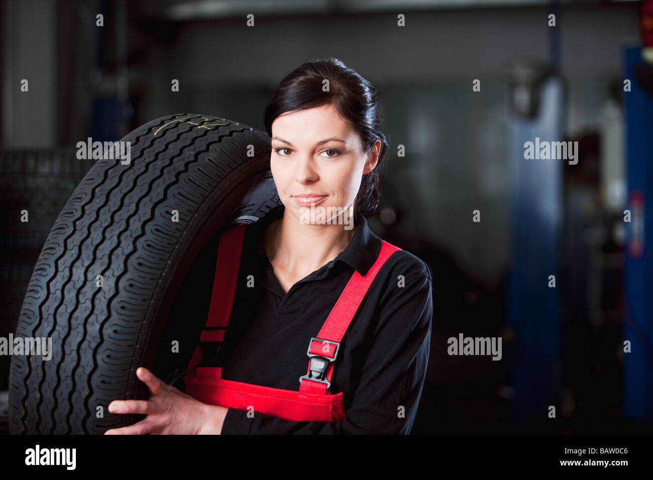 portrait of female mechanic carrying tire Stock Photo