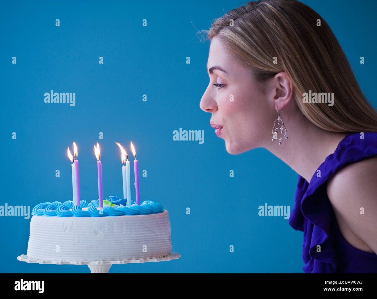 Young woman blowing candles on birthday cake, studio shot Stock Photo