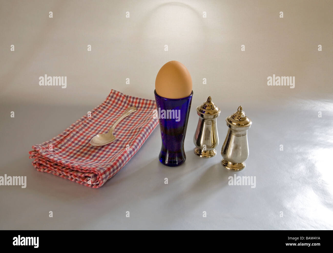 A soft boiled egg in an egg cup with salt and pepper shakers Stock