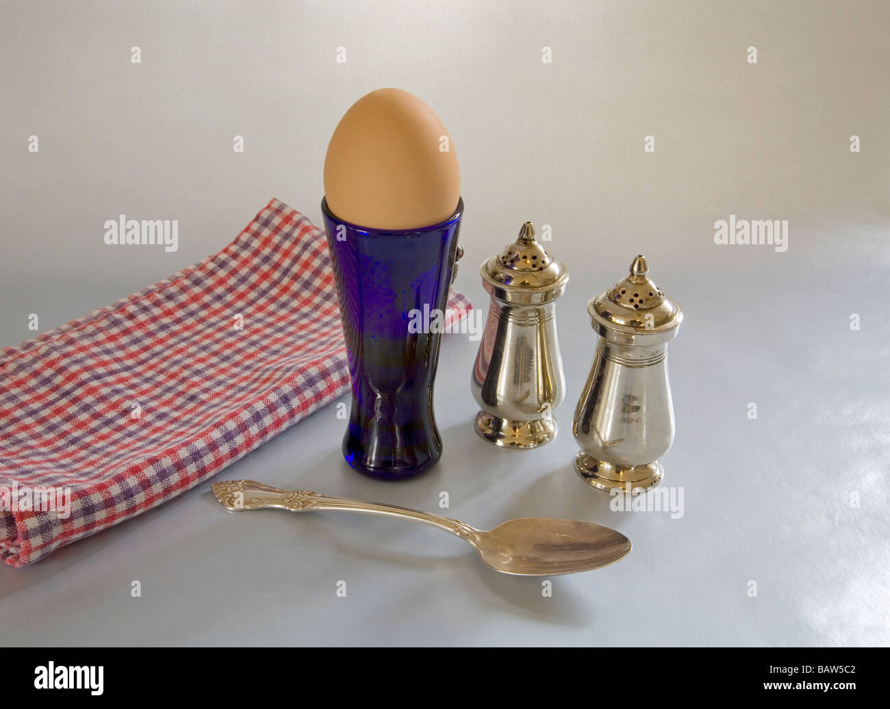 A soft boiled egg in an egg cup with salt and pepper shakers Stock