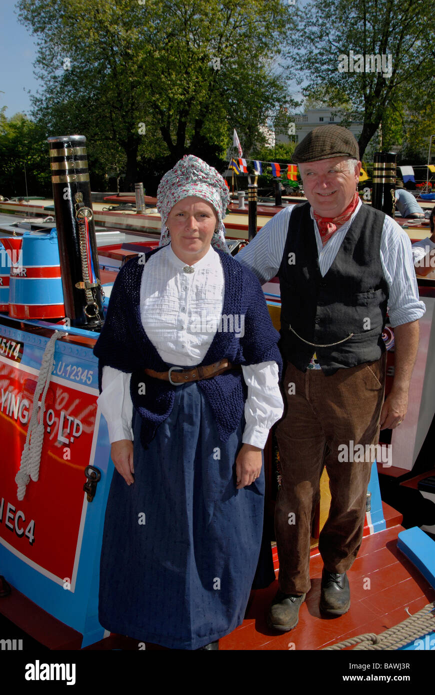 Man and woman in traditional Victorian narrowboat costume standing on the stern of their working narrowboat, London, England Stock Photo