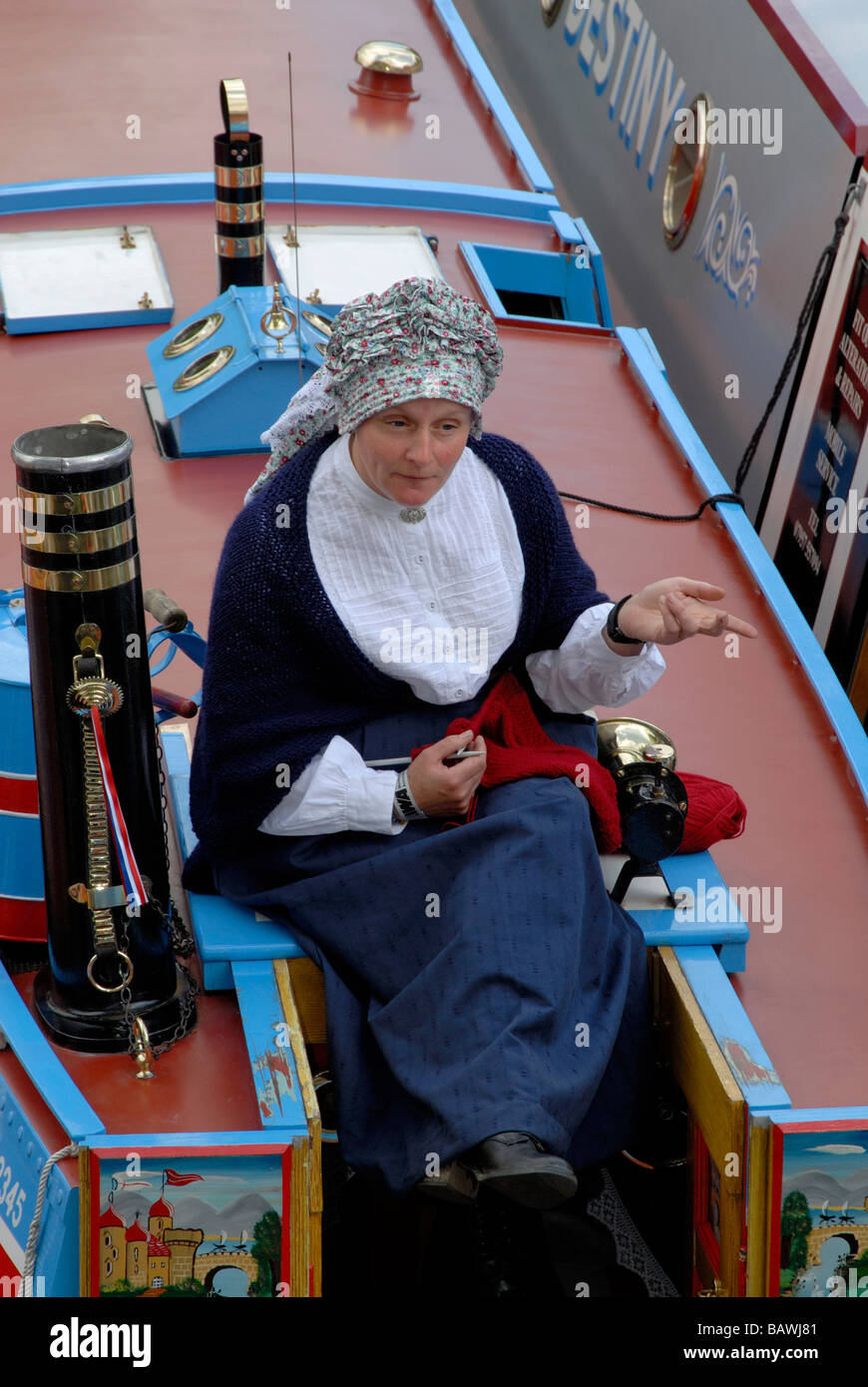 Woman in traditional Victorian narrowboat costume with her knitting sitting on hatch of working narrowboat, London, England Stock Photo