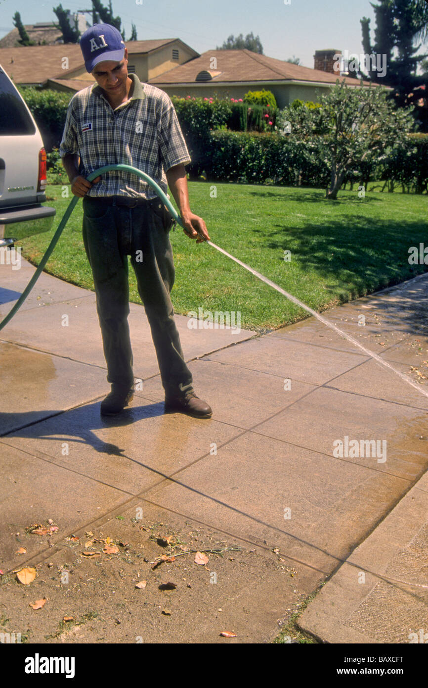 man hose clean driveway street sidewalk yard maintain water waste Stock