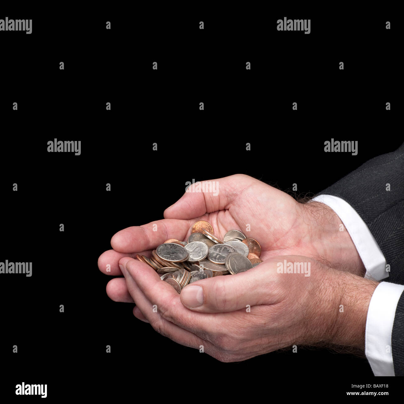 A man cups his hands as he holds a pile of coins Image was shot against a black backdrop and is not a cutout Stock Photo