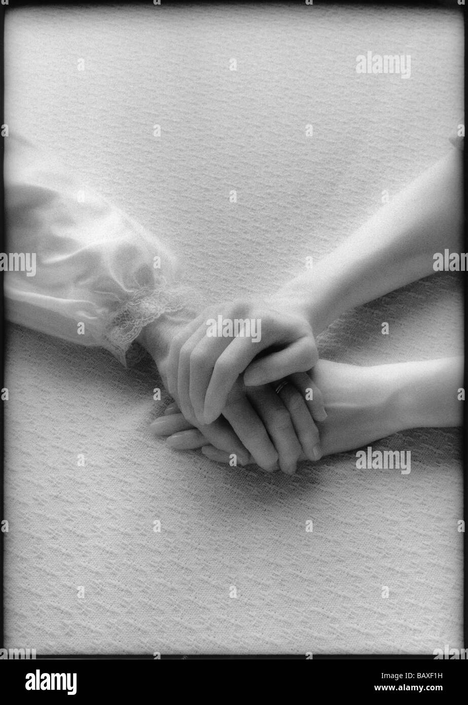 Grayscale image of clasped hands of elderly woman and caregiver on fabric background Stock Photo