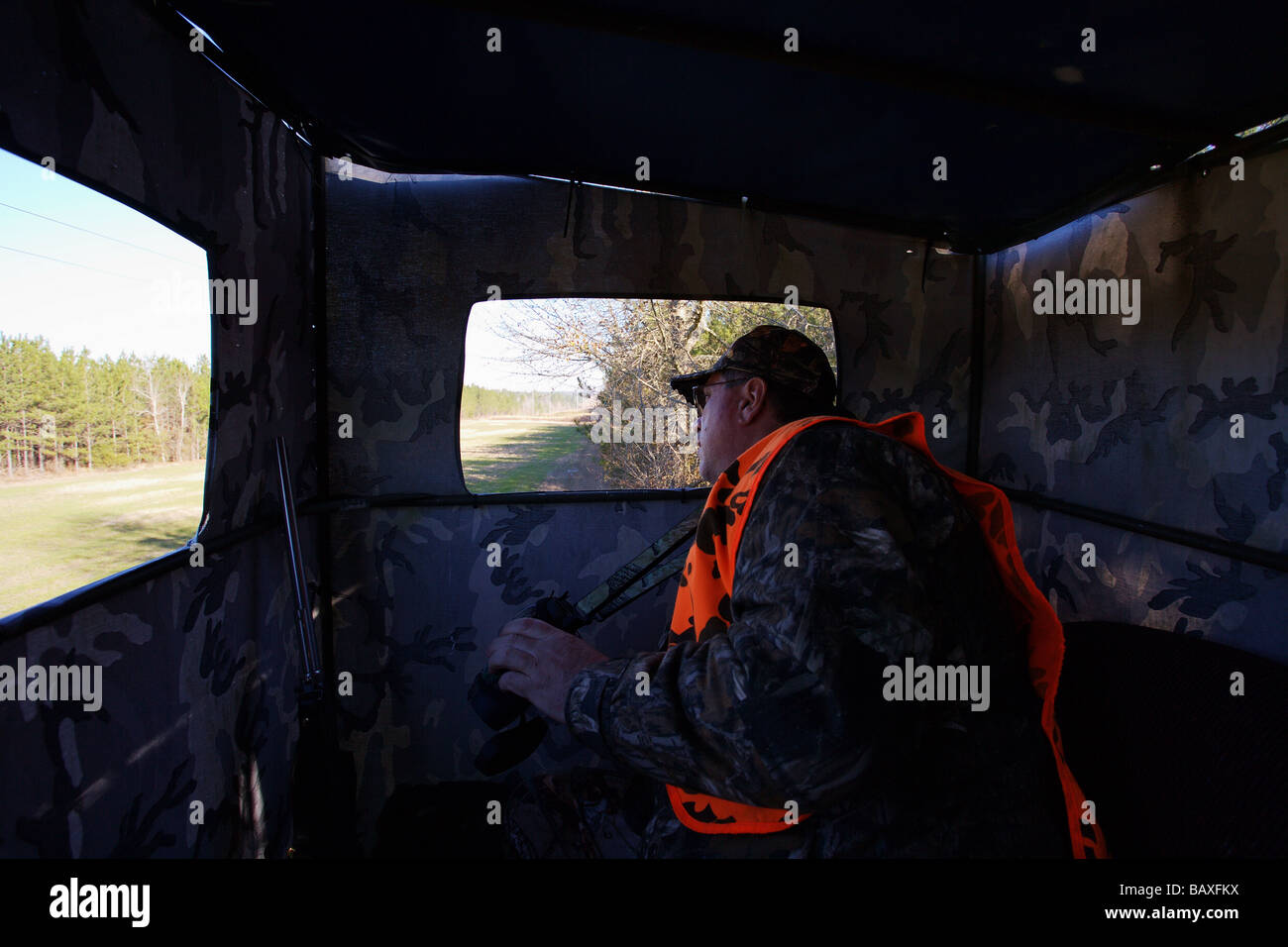 HUNTER SITTING IN RAISED BLIND LOOKING FOR GAME ORANGE BLAZE VEST
