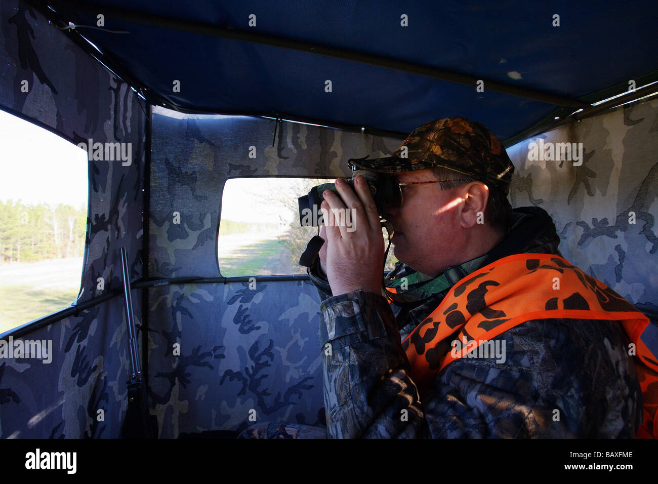 HUNTER SITTING IN RAISED BLIND LOOKING FOR GAME ORANGE BLAZE VEST
