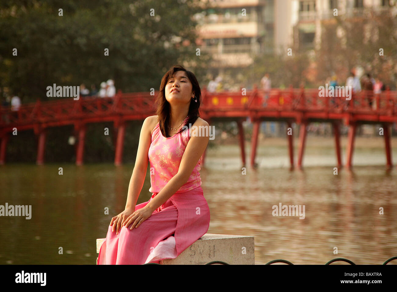 nice young girl with traditional dress posing for a photo with The Huc Bridge on Hoan Kiem lake in Hanoi Vietnam Asia Stock Photo