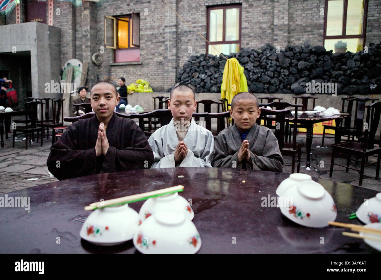 Young monks eating lunch, coal used cooking in the background, during birthday celebrations for Wenshu, Mount Wutai, Wutai Shan, Stock Photo
